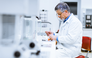 stock image of older scientist in lab coat sitting at bench